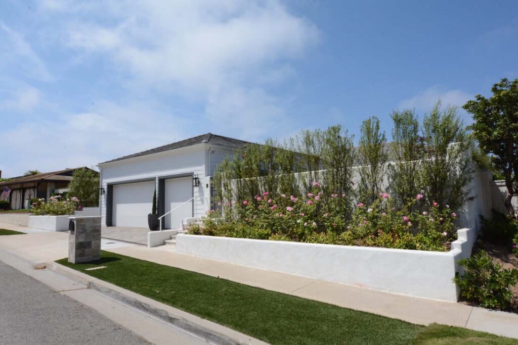 curbside view of traditional beach home with low white retaining wall garage and private courtyard in corona Del Mar